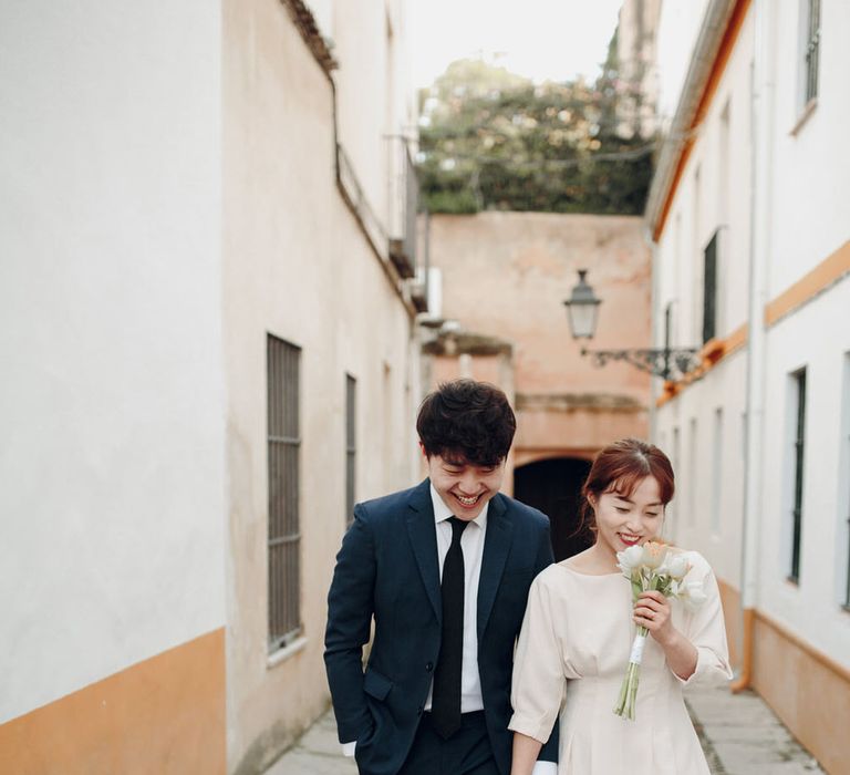 Couple walk down street holding hands, woman smelling lily bouquet