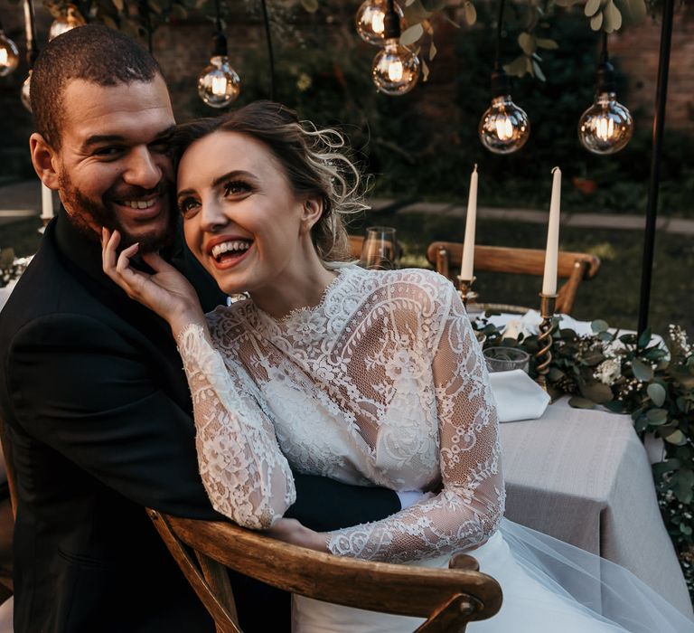 Black tie wedding with bride and groom laughing sitting at their festoon lit wedding reception table 