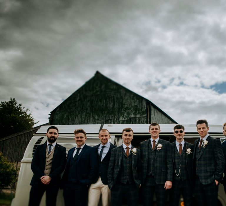 Groomsmen in three-piece navy and navy checked suits standing in front of a camper van 