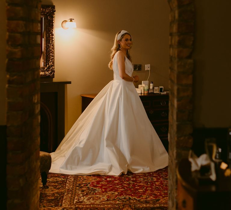 Bride is seen through doorway before wedding ceremony wearing Suzanne Neville bridal gown with full skirt