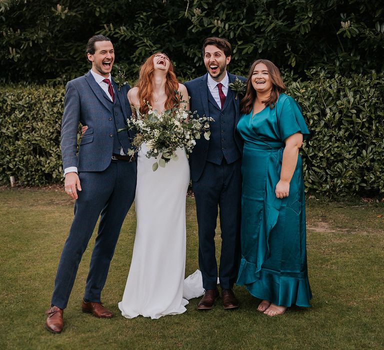 Bride and groom with their best man in a navy wool suit and bridesmaid in a satin teal wrap dress 