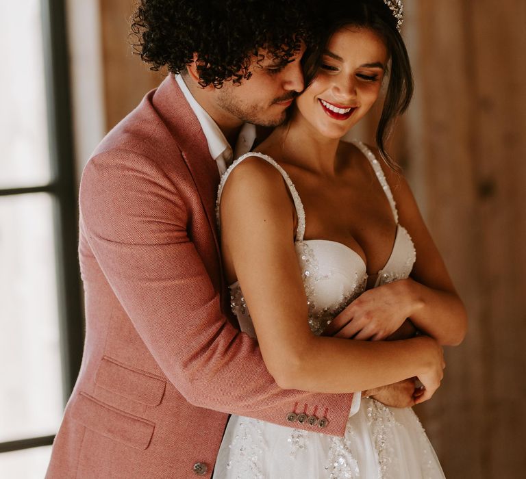 Groom in a pink tweed jacket embracing his bride in a thin strap wedding dress with corset bodice 