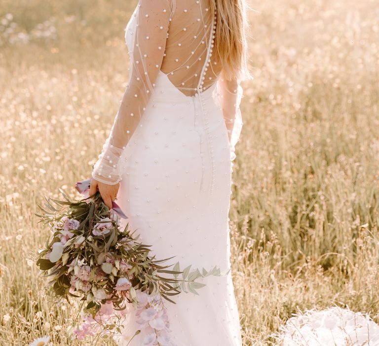 Bride stands within golden fields on her wedding day carrying floral bouquet