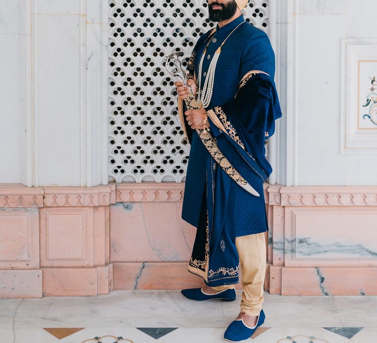 Groom wears royal blue on his wedding day whilst holding sword for Punjabi wedding