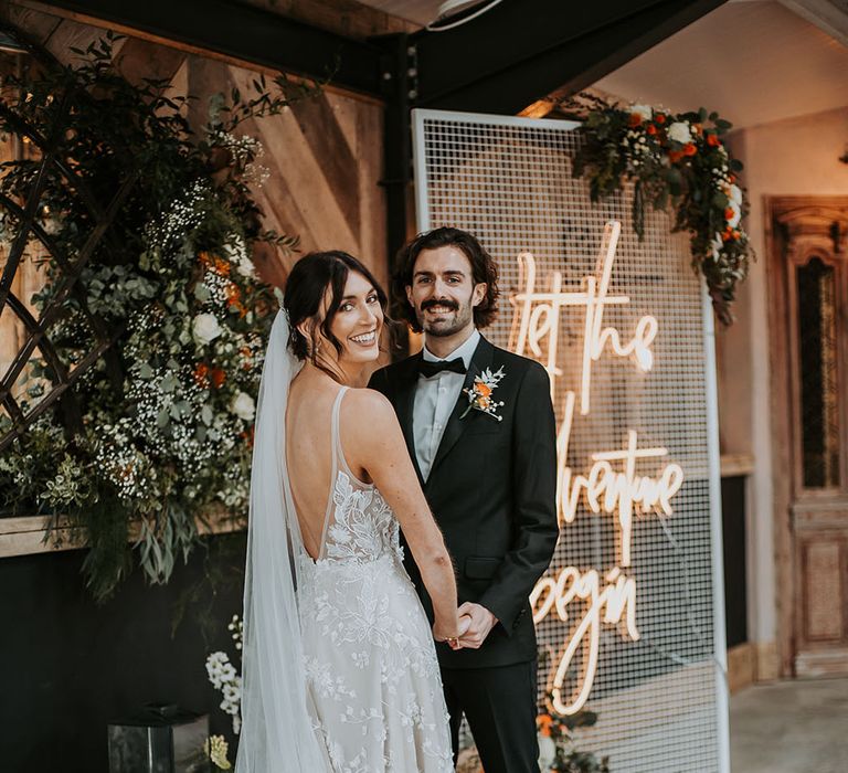 Bride in a Made With Love Bridal Carla A-line gown with appliqué detail accessorised with a cathedral length veil holding hands with her groom in a tuxedo 