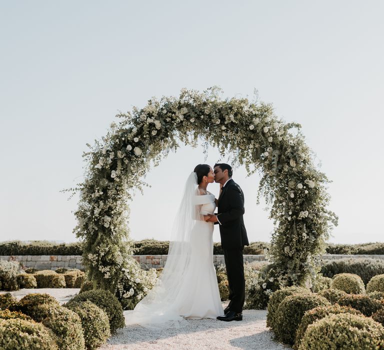 Bride & groom kiss in front of floral installation at the end of the aisle for Greek wedding | Hannah MacGregor Photo & Film