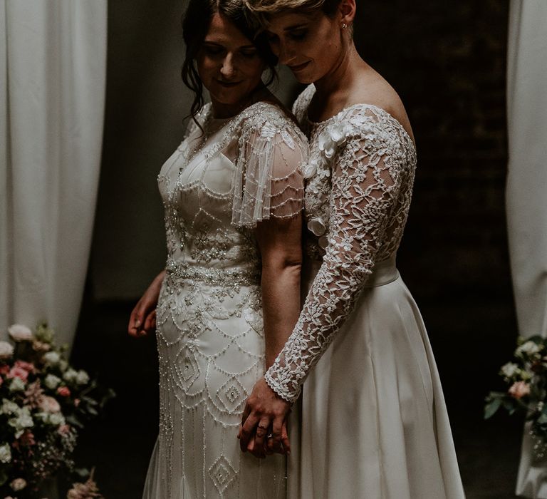 Bride with short blonde hair wearing a wedding dress with lace long sleeves embracing her bride in a vintage inspired wedding dress 