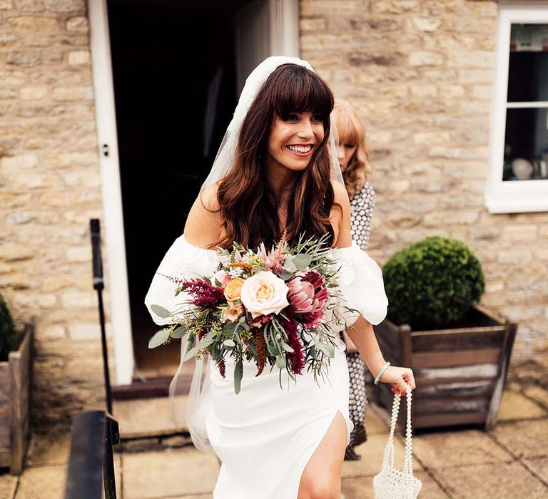 Bride in a strapless wedding dress with lace veil holding her wedding bouquet and a beaded bag