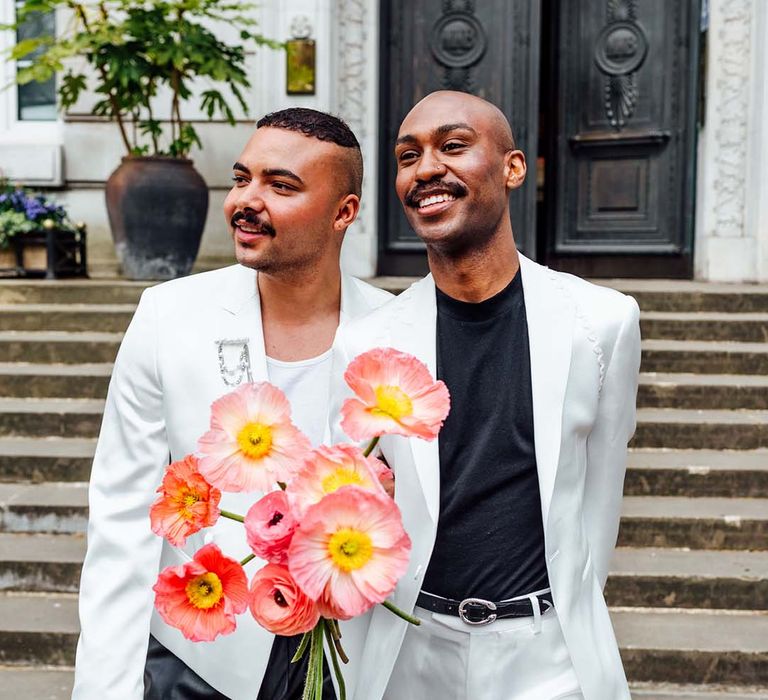 Black grooms in monochrome suits with coral ranunculus and anemones 