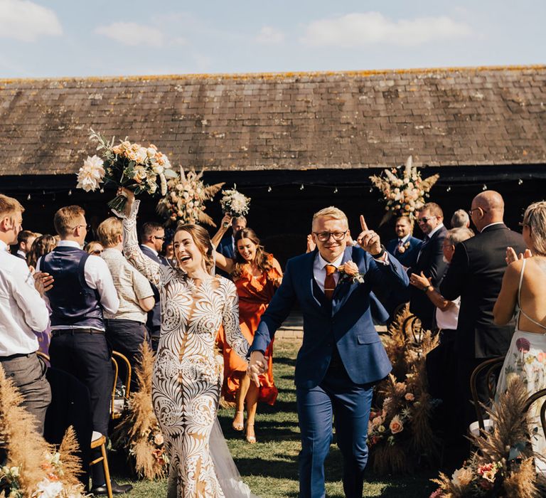 Boho Bride & Groom holding hands at Elmley Nature Reserve barn wedding with pampas grass arrangements