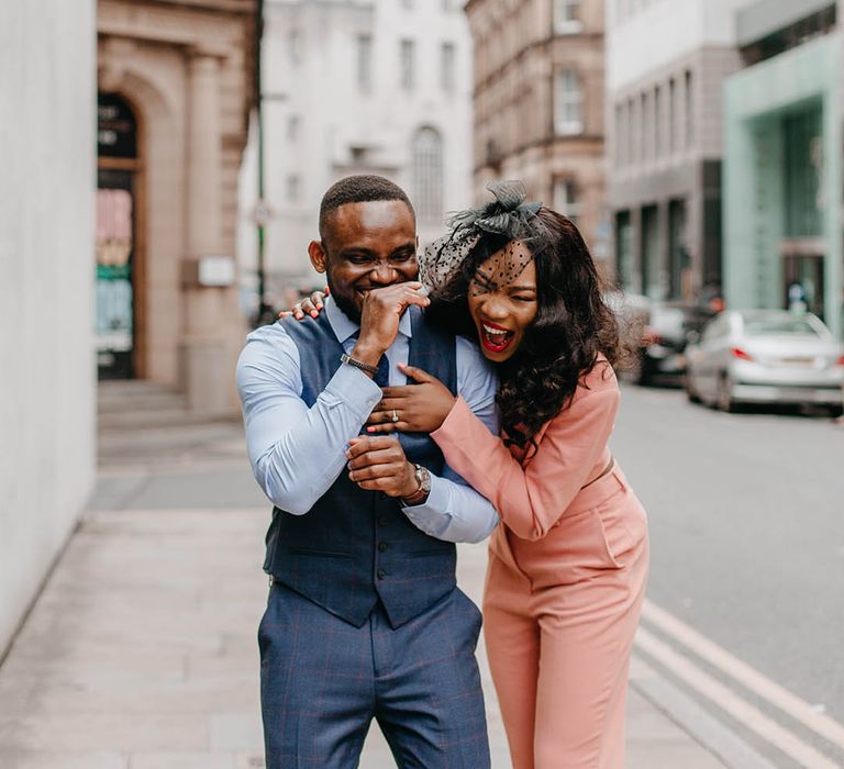 Bride & groom laugh as bride wears salmon coloured suit 