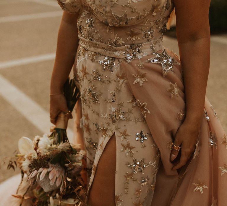 Bride walks with her floral bouquet in hand and holds detachable skirt to the side