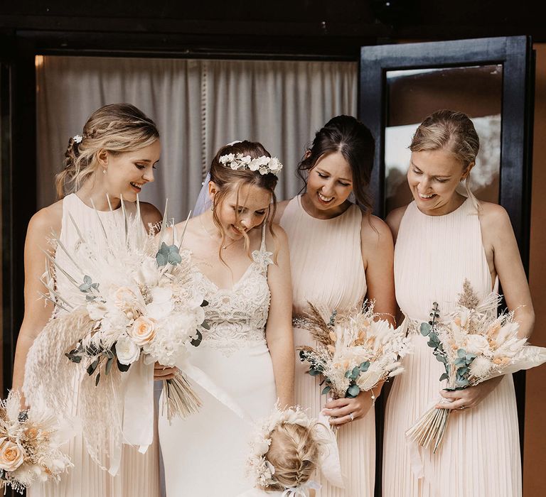 Bride stands with her bridesmaids who wear pale pink gowns as they smile lovingly at her daughter