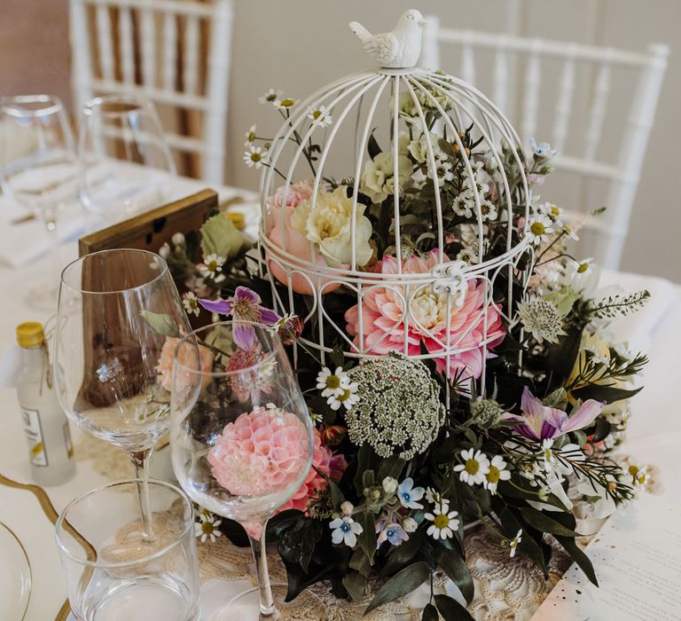 Bright summer floral cage centrepiece for rustic chic wedding reception with glassware and gold rimmed plates