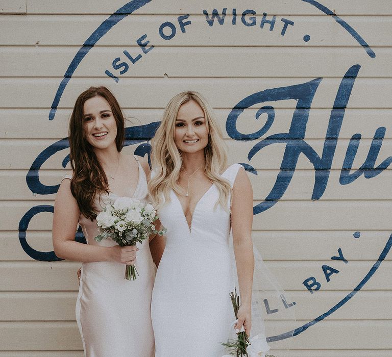 Bride and bridesmaid in champagne dress both clutch white flower bouquets