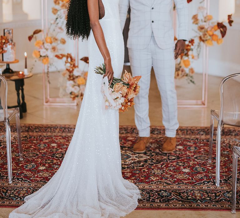 Stylish Black bride in a sparkly wedding dress and Black groom in a beige check suit at their Kirtlington Park wedding with orange flowers