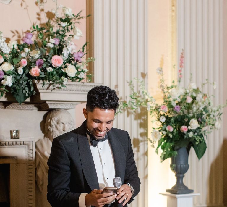 Groom wears black tie and reads speech during wedding reception