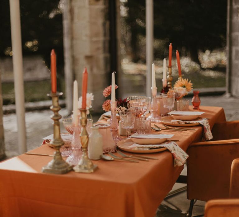 wedding tables cape with orange tablecloth, coloured glassware and taper candles 