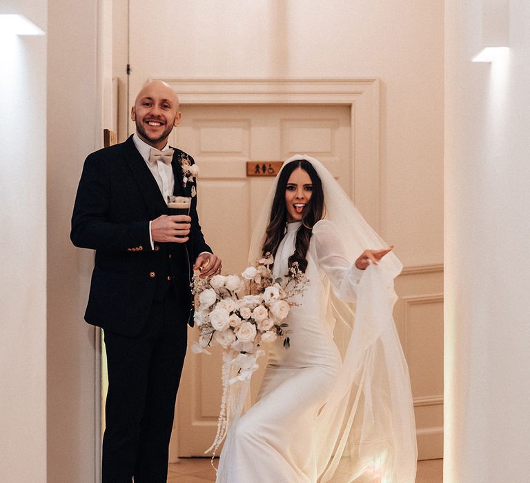 Bride in a satin fitted wedding dress with high neck and long sleeves and groom in a black wedding suit 