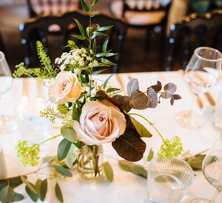 Pink roses and green foliage in milk bottles on white tablecloth tablescape