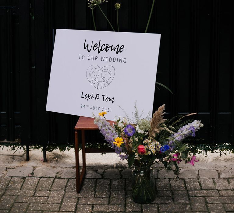 Simple welcome sign for wedding with personalised sketch, name and date with colourful flower bouquets