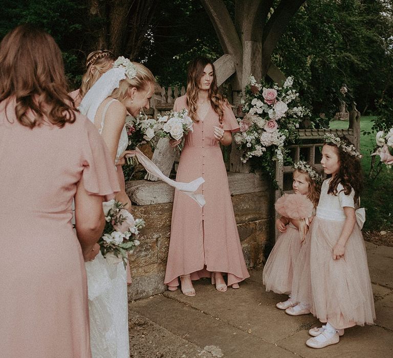 Bridesmaids in simple muted pink button up bridesmaid dresses with flower girls in white and pink tulle dresses with a bow 