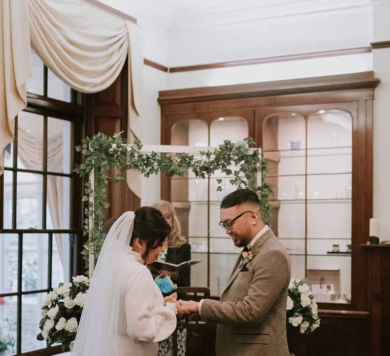 Exchanging rings - Bride in Vanessa Cocchiaro wedding dress with Jimmy Choo heels and groom in Tru Clothing outfit with GH Bass x Maharishi