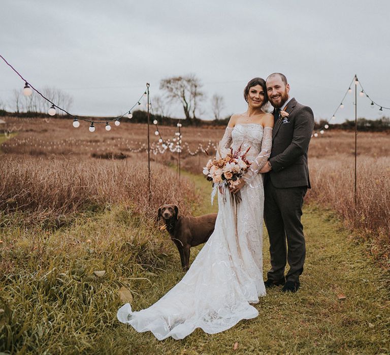 Groom smiles at the camera with bride in Zavana Couture wedding dress and their pet dog