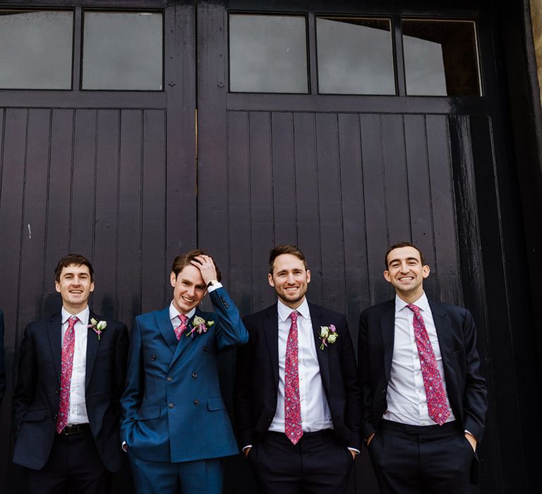 Groom in double breasted blue suit and pink and blue patterned tie with groomsmen in matching ties and darker suit jackets