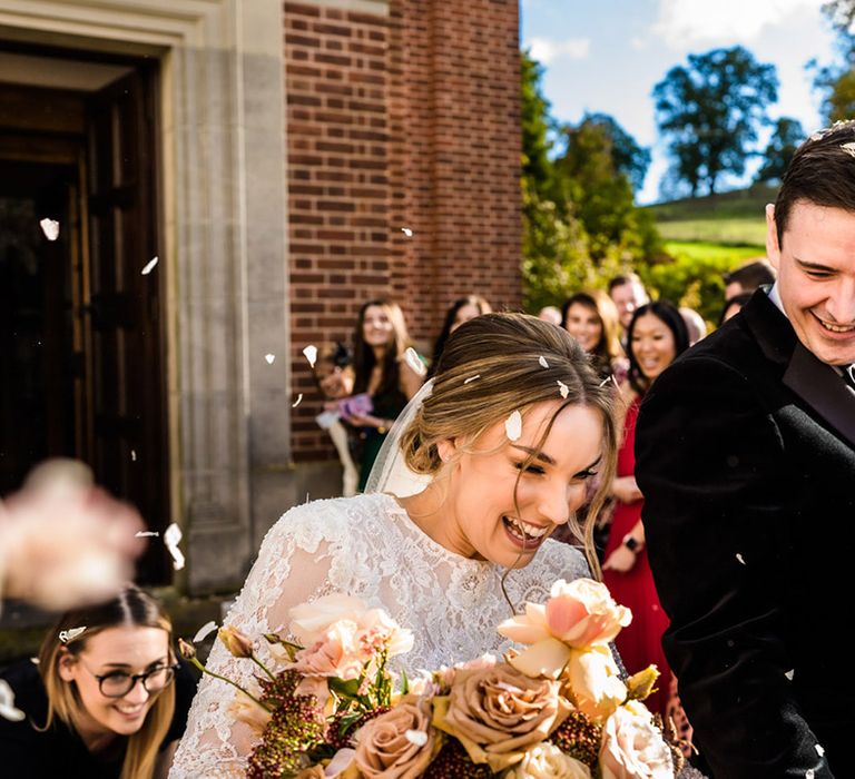 Bride in long sleeve lace wedding dress has confetti exit with groom in black tie 