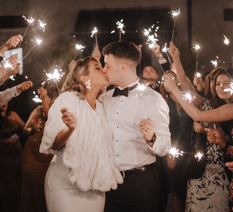 Sparkler exit for bride wearing white fur cover-up and groom in black tie