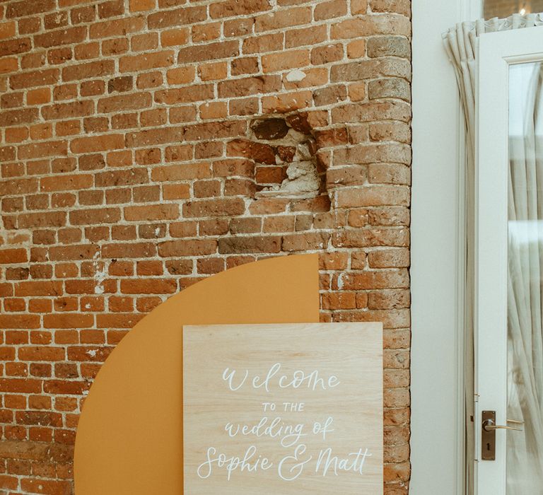 Wooden welcome wedding sign with orange and neutral arch boards and moss flower arrangement with roses 