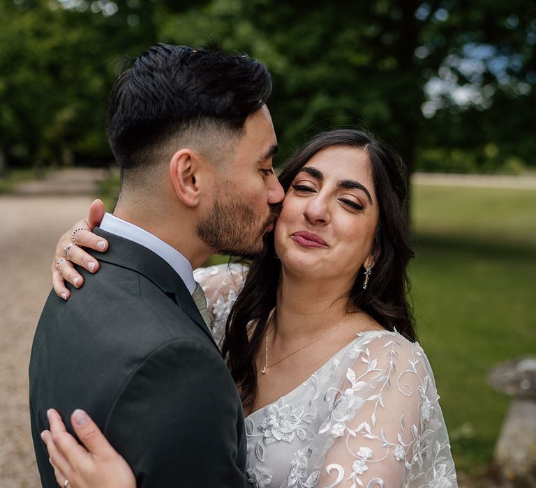 Groom kisses his bride who wears floral lace embellished boho chic wedding dress