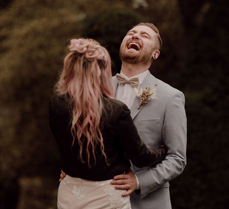 Bride wears black denim jacket with her groom wearing pale grey three piece suit outdoors 