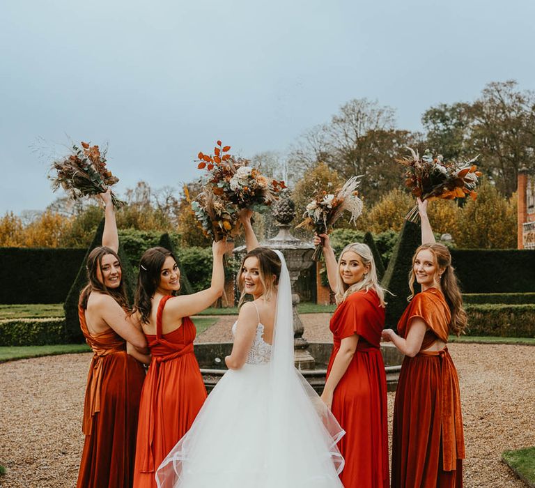 Bridesmaids in burnt orange dresses with bride in layered tulle princess skirt all holding matching autumnal bouquets 