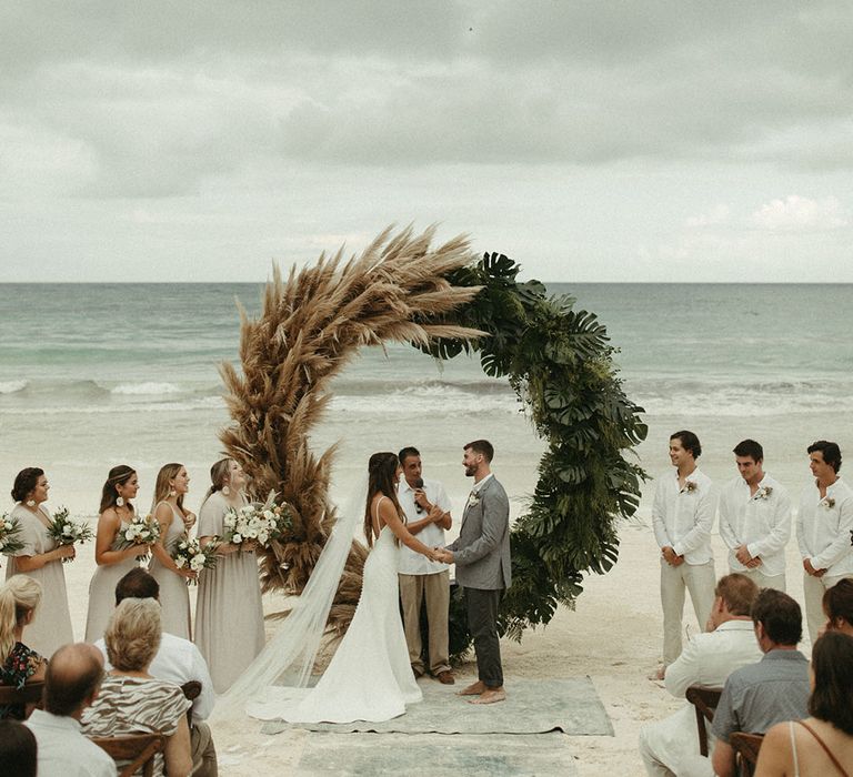 Bride and groom have a beach wedding ceremony with a half and half pampas grass moongate 