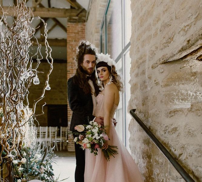 Bride in a pink strapless wedding dress by Felisiti Greis standing on the steps at The Tithe Barn Hooton Pagnell with her groom in a tuxedo 