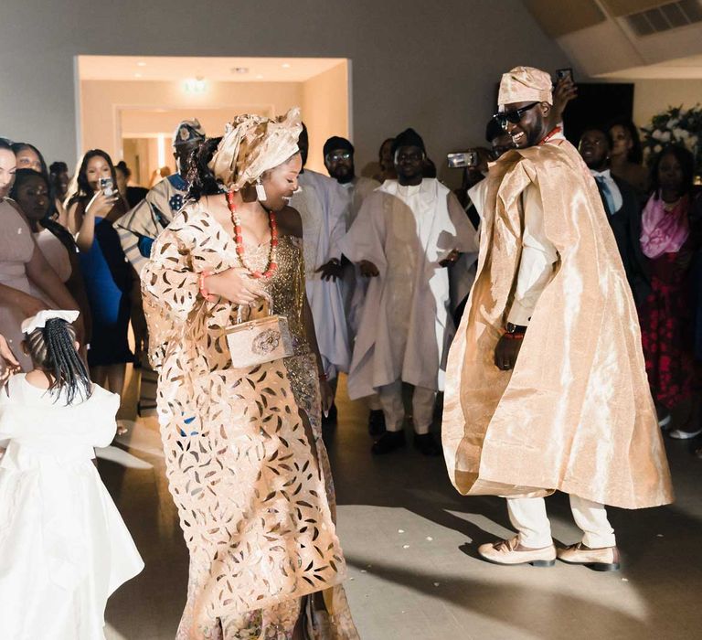 Bride & groom wearing matching coloured Nigerian traditional formal attire dance with one another during reception