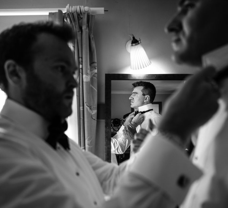 Groom has his black tie done up by groomsmen on the morning of his wedding day