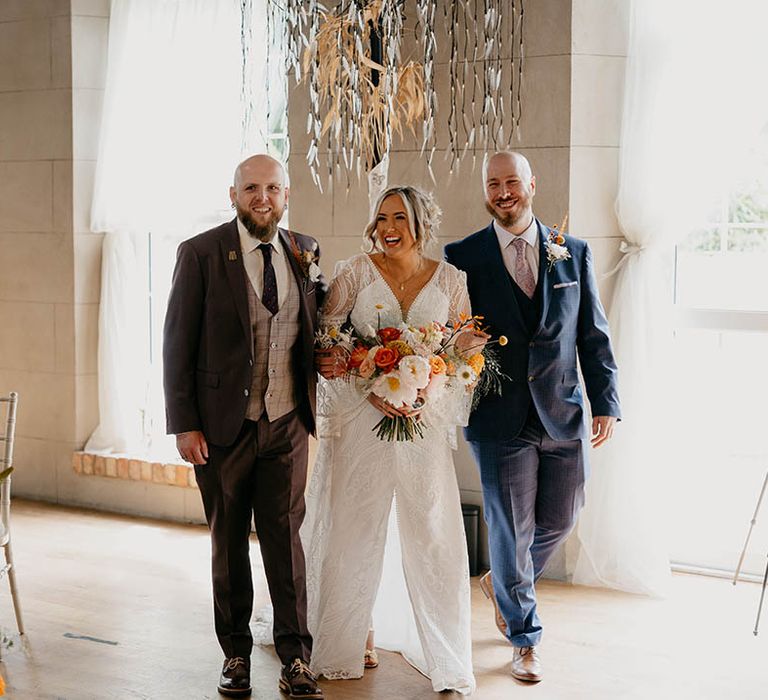 The bride's brother and best friend walk the bride in a boho wedding dress from Bibiluxe Studio down the aisle 