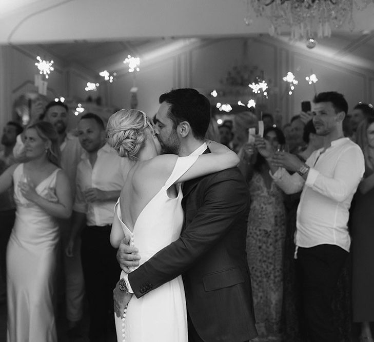 Bride & groom dance as wedding guests hold sparklers around them in black & white image