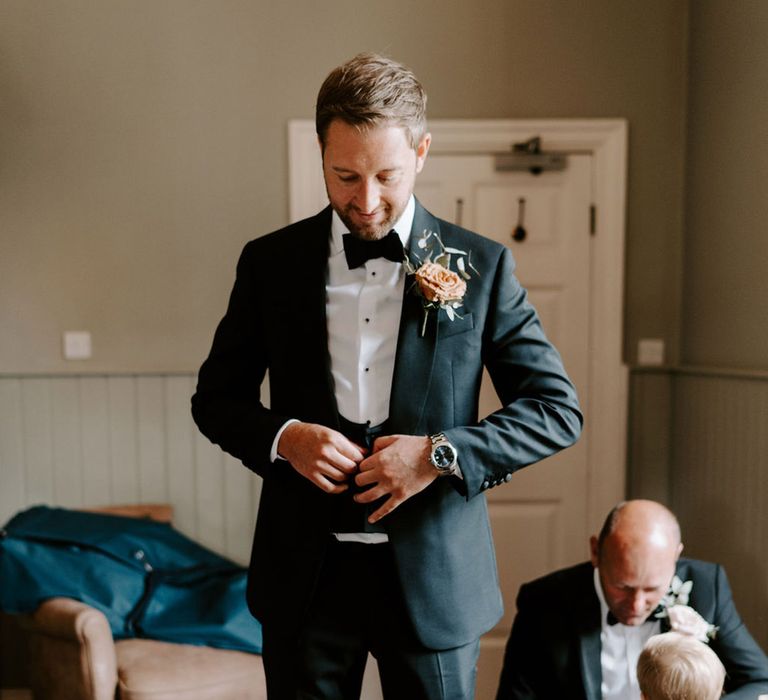 Groom gets ready for the wedding as he gets into his classic black tie 