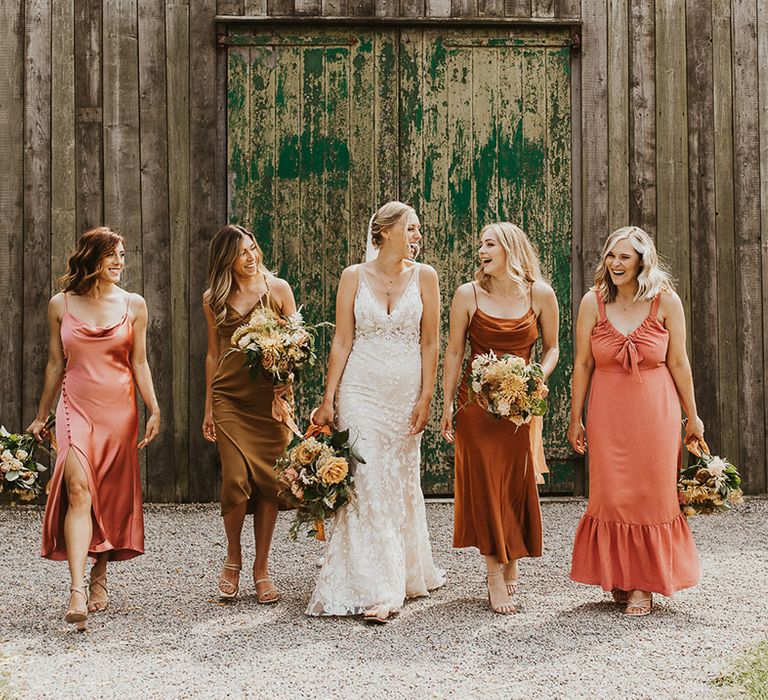 Bride in a lace Made With Love wedding dress standing with her bridesmaids in mismatched coloured dresses 