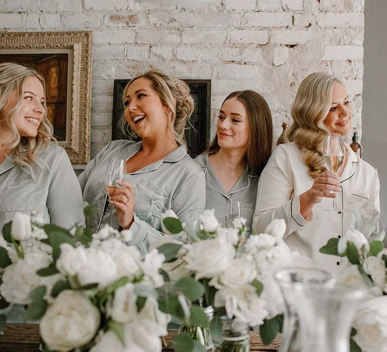 Bridesmaids & bride wear matching pyjamas whilst stood beside white floral bouquets 