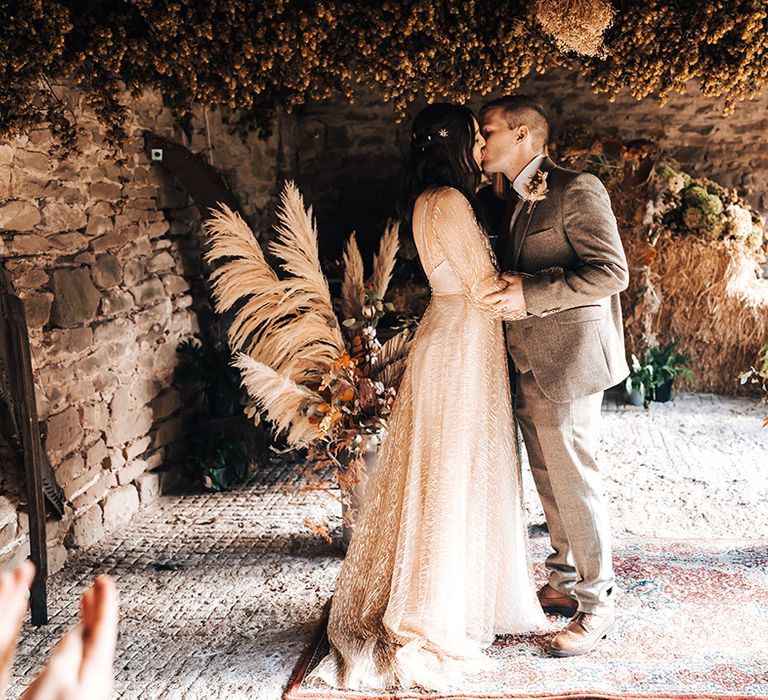 Bride & groom kiss beneath dried foliage as pampas grass flower bouquets surrounded them