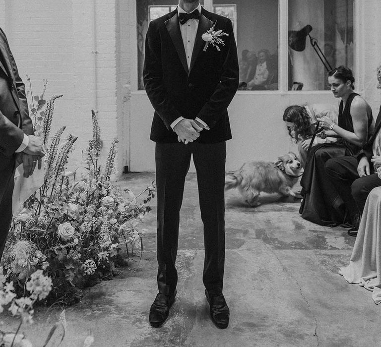 Groom in black tux with bow tie and boutonniere waiting for bride at the end of the alter at Hackney Studios