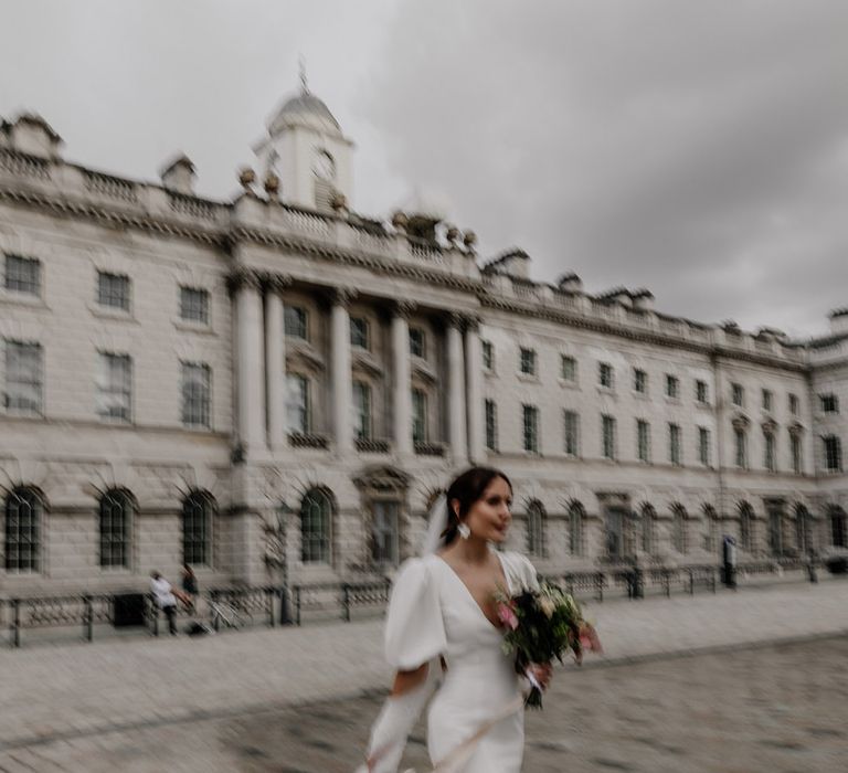 Bride in modern front slit v neck wedding dress with puff sleeves and neutral toned bouquet