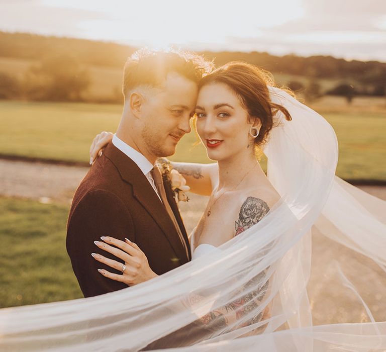 Bride's veil blows around herself and her groom during golden hour couples portraits