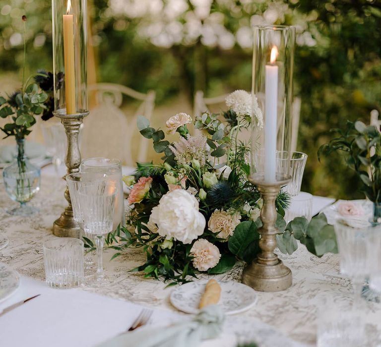 Beautiful Italian tablescape with ribbed glassware, gold candlestick holders and flower arrangements that include thistles, peonies, carnations and wildflowers