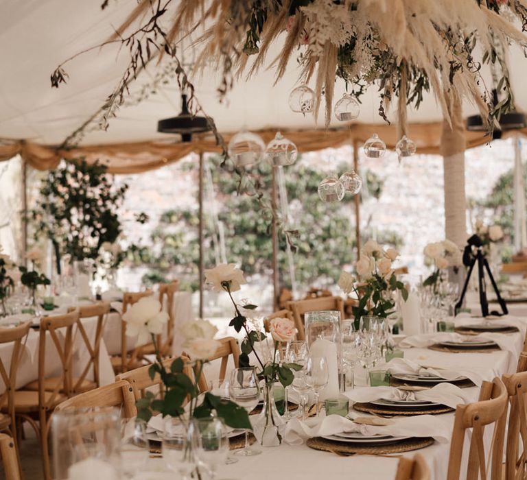 Flower installation with pink roses and flowers with pampas grass over the tables with a green and white theme 